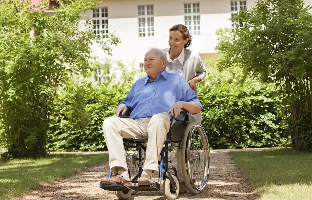 Frau von Seniorenbetreuung zuhause schiebt Rollstuhl